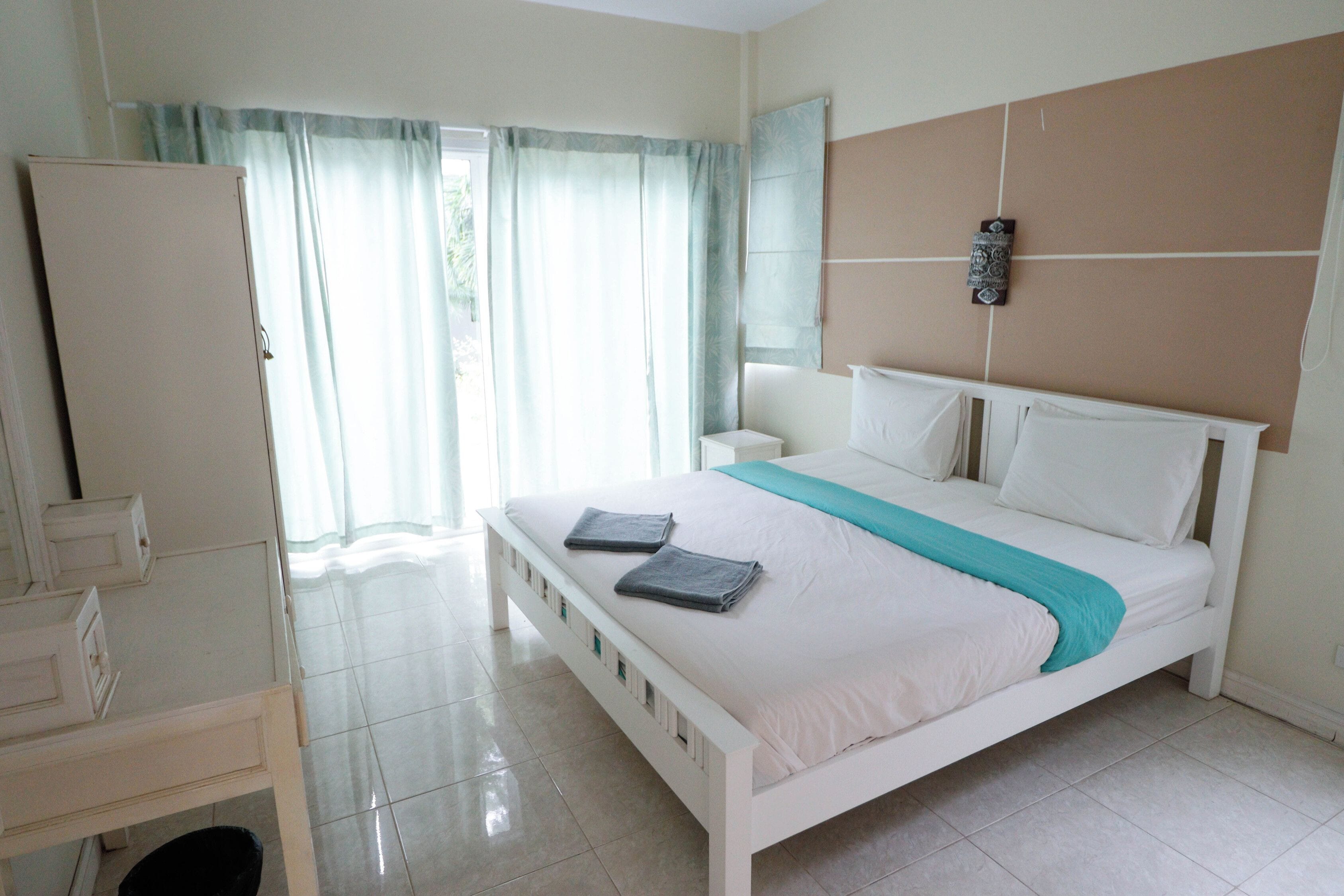 Un dormitorio con cama, mesita de noche, armario y ventana con cortinas.