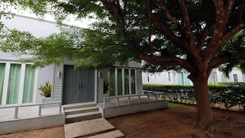 Uma casa de dois andares com varanda frontal, degraus que levam à porta e uma grande árvore na frente.