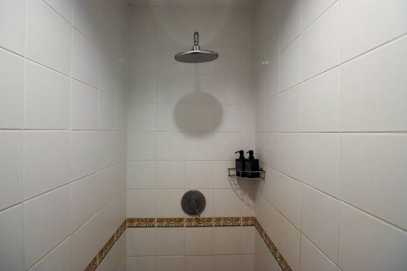A shower with a handheld showerhead, a soap dispenser, and a small shelf.