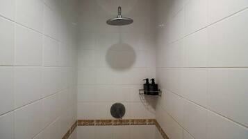 A shower with a handheld showerhead, a soap dispenser, and a small shelf.