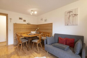 A cozy living room with a wooden dining table, four chairs, a grey sofa with red cushions, and a wall with framed artwork. - Quiet and charming apartments with beautiful views (Schruns-Tschagguns)