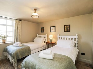 Ein Zimmer mit zwei Einzelbetten, einem fensterbelaubten Fenster, einer Lampe auf einem Nachttisch und einer Deckenleuchte.
