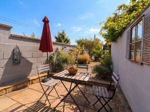 Un pati amb taula i cadires, un parasol vermell i un jardí amb plantes diverses.