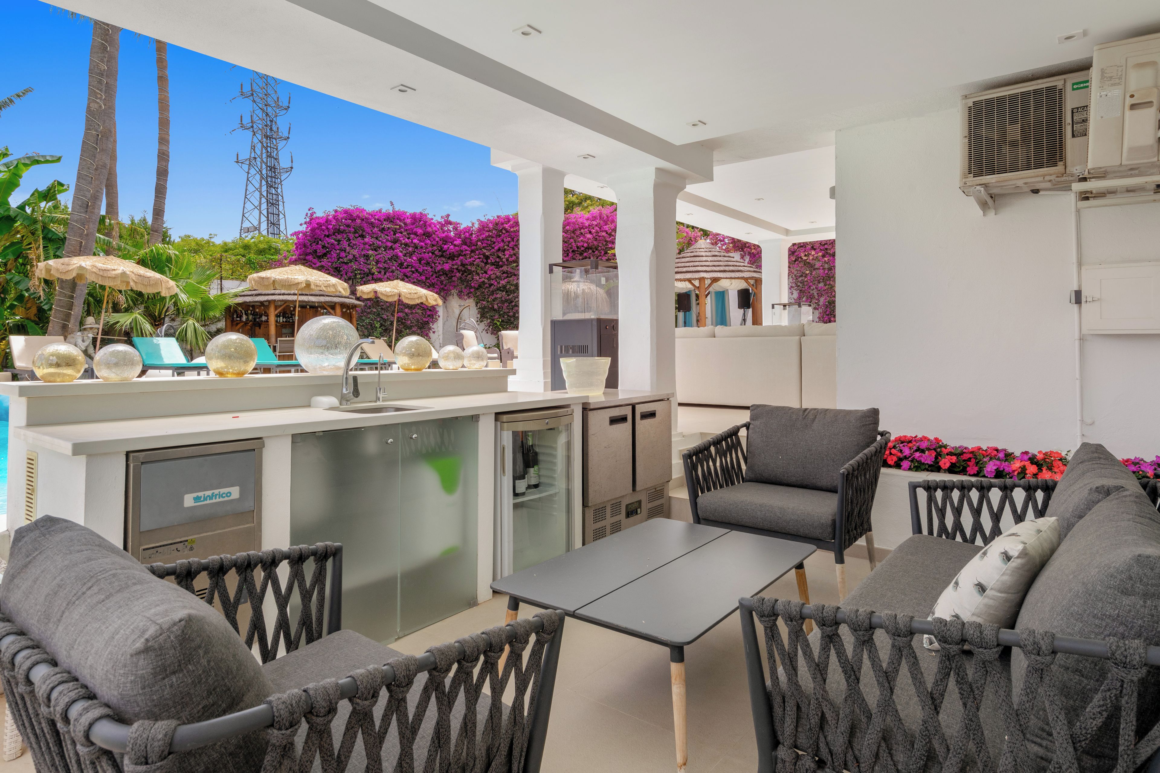 An outdoor patio area with a bar, seating, and a view of the sky and vegetation.