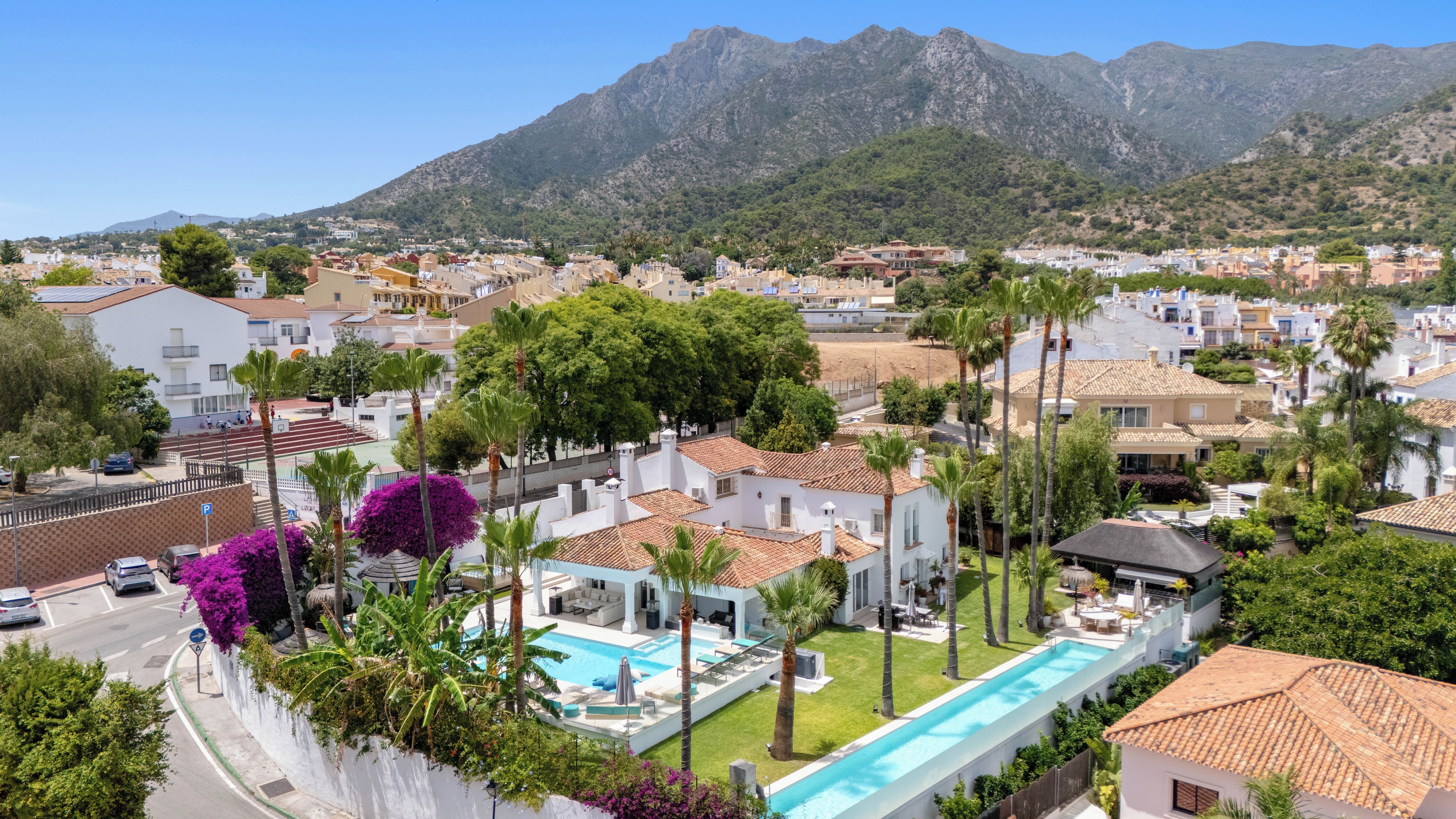 A residential area with a swimming pool, palm trees, and houses with red-tiled roofs.
