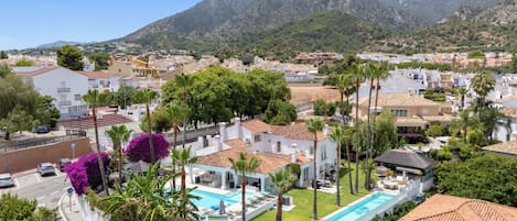 A residential area with a swimming pool, palm trees, and houses with red-tiled roofs.