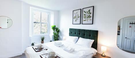 A hotel room with a bed, bedside table, lamp, window, and wall-mounted mirror.