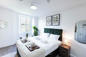 Habitación de hotel con cama, mesita de noche, lámpara, ventana y espejo en la pared.