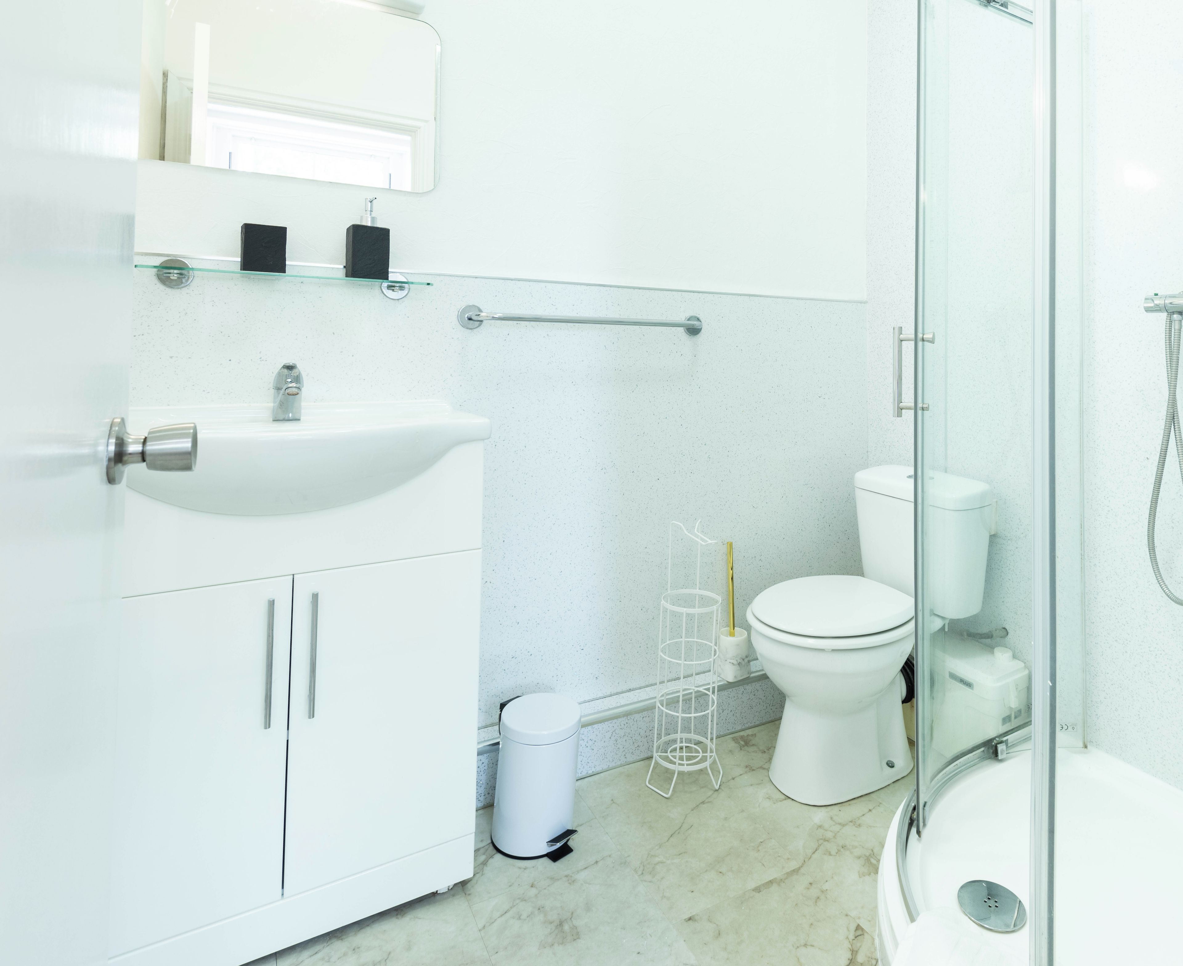 Un bagno moderno con lavandino, water e zona doccia, tutti in bianco.