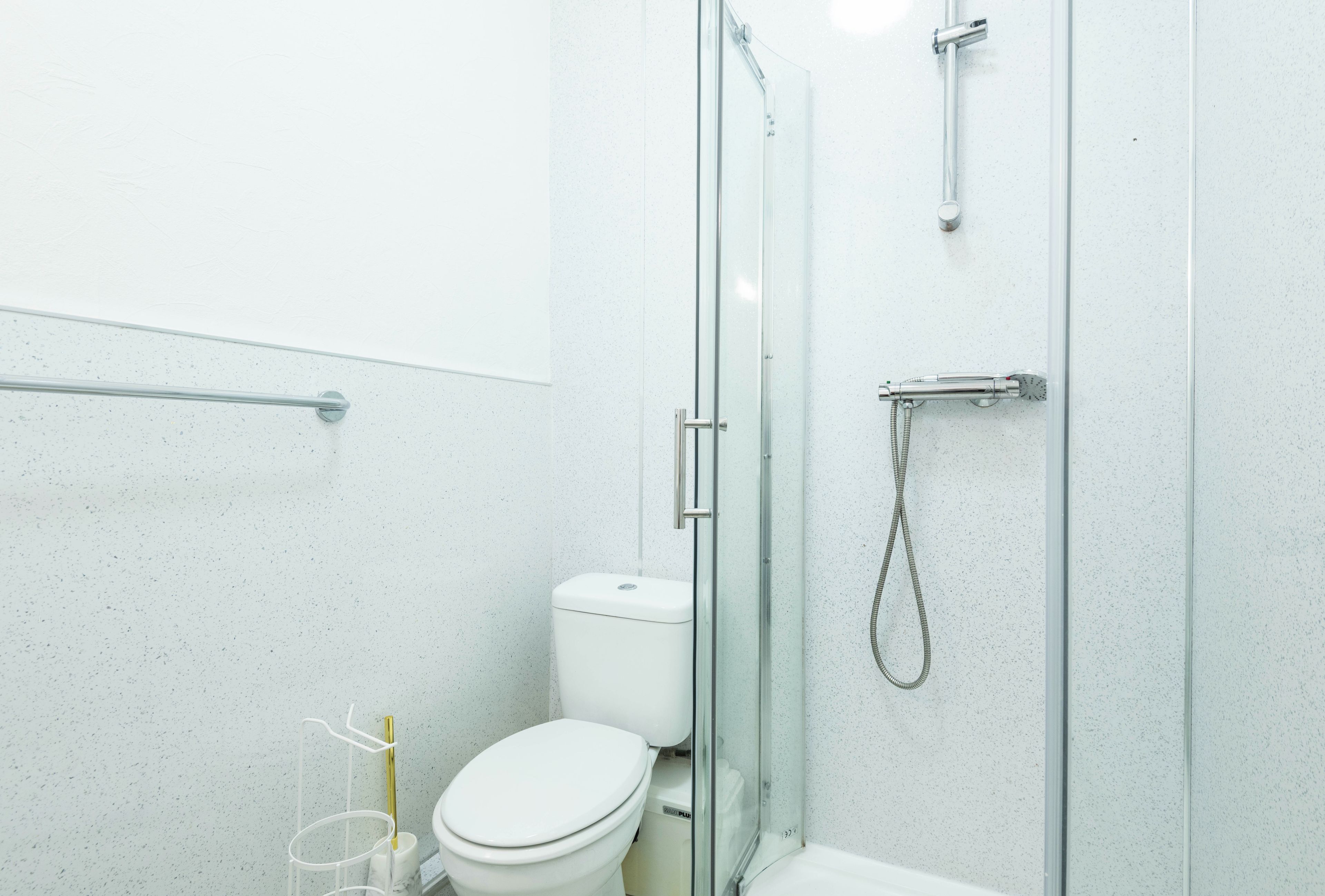 A modern bathroom with a glass-enclosed shower, a white toilet, and a handrail.