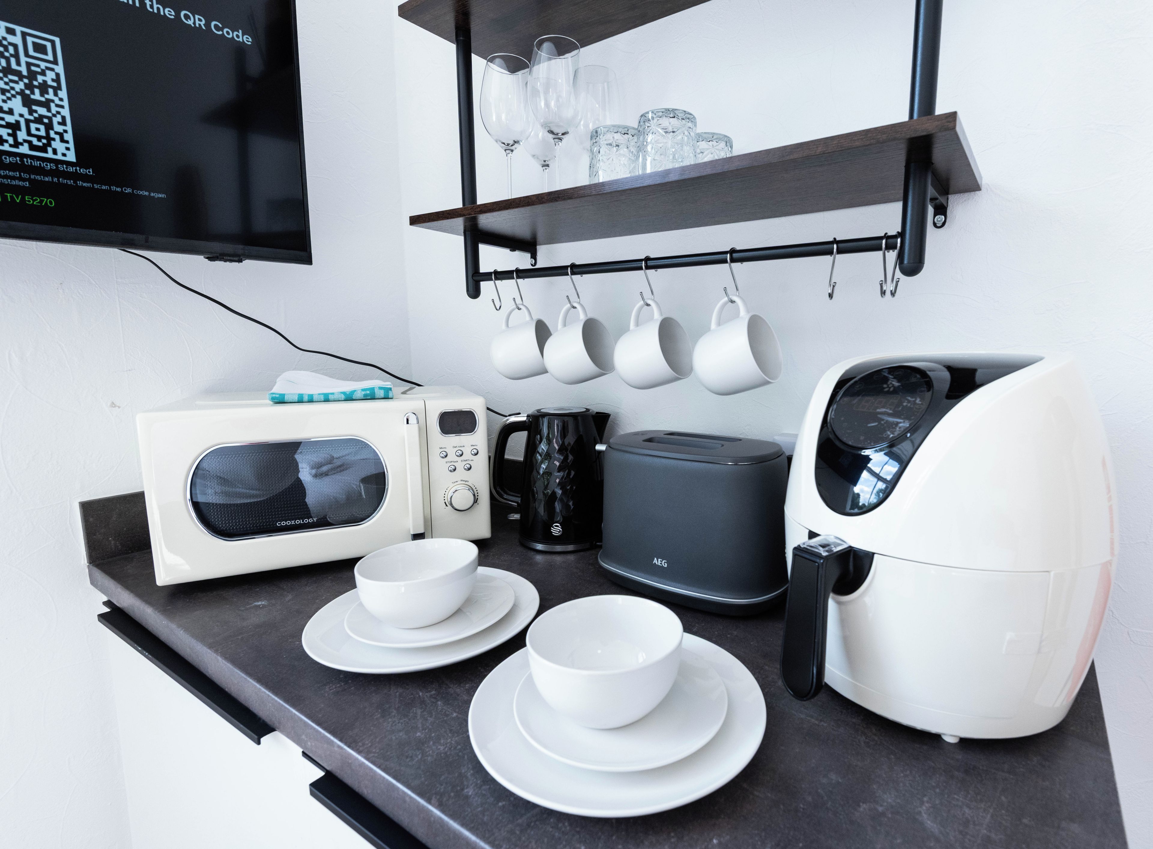 A kitchenette with a microwave, toaster, coffee maker, and a shelf with cups and glasses.