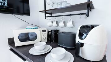 A kitchenette with a microwave, toaster, coffee maker, and a shelf with cups and glasses.