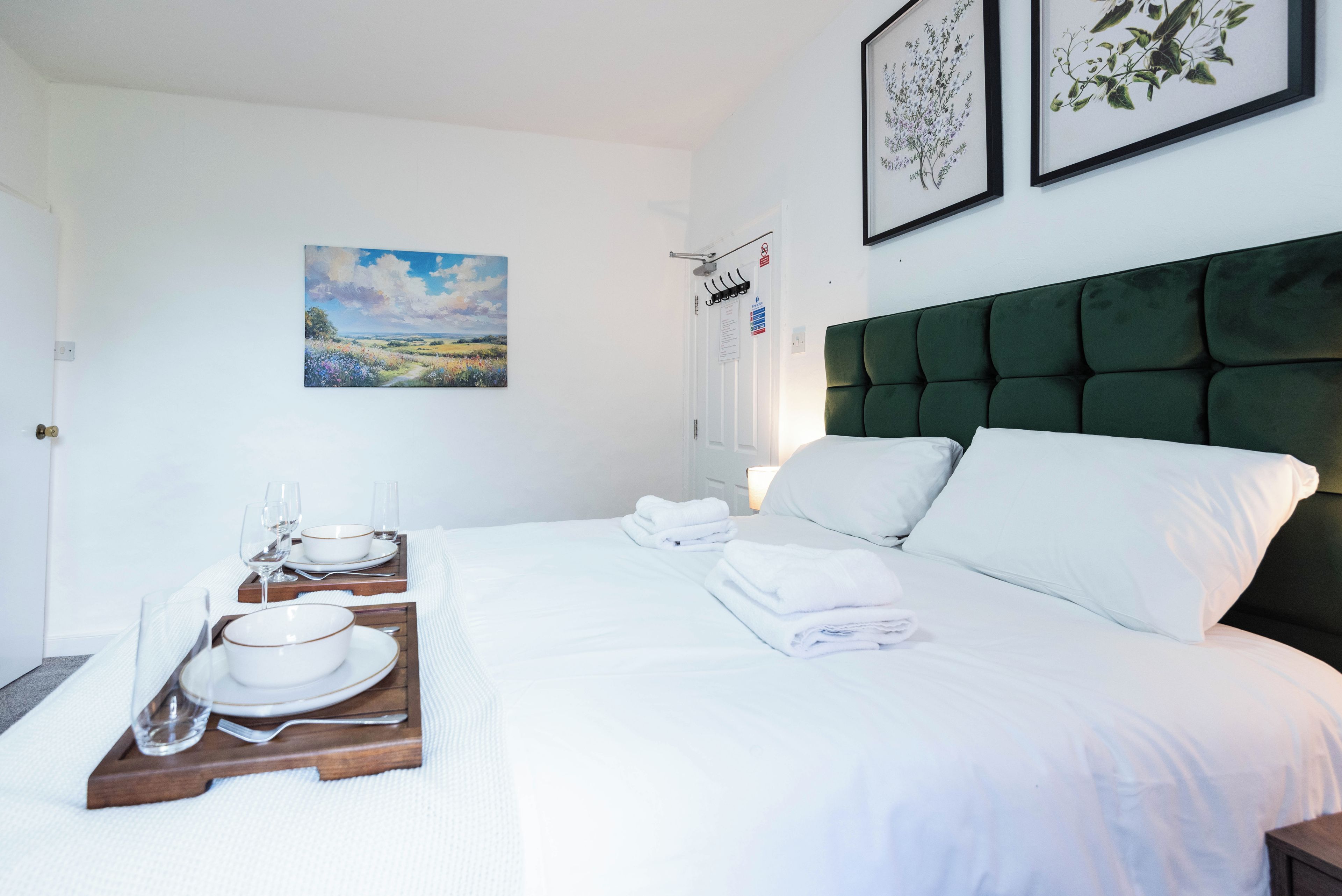 Une chambre d’hôtel avec un lit soigneusement fait, un tableau au mur et une illustration botanique encadrée.