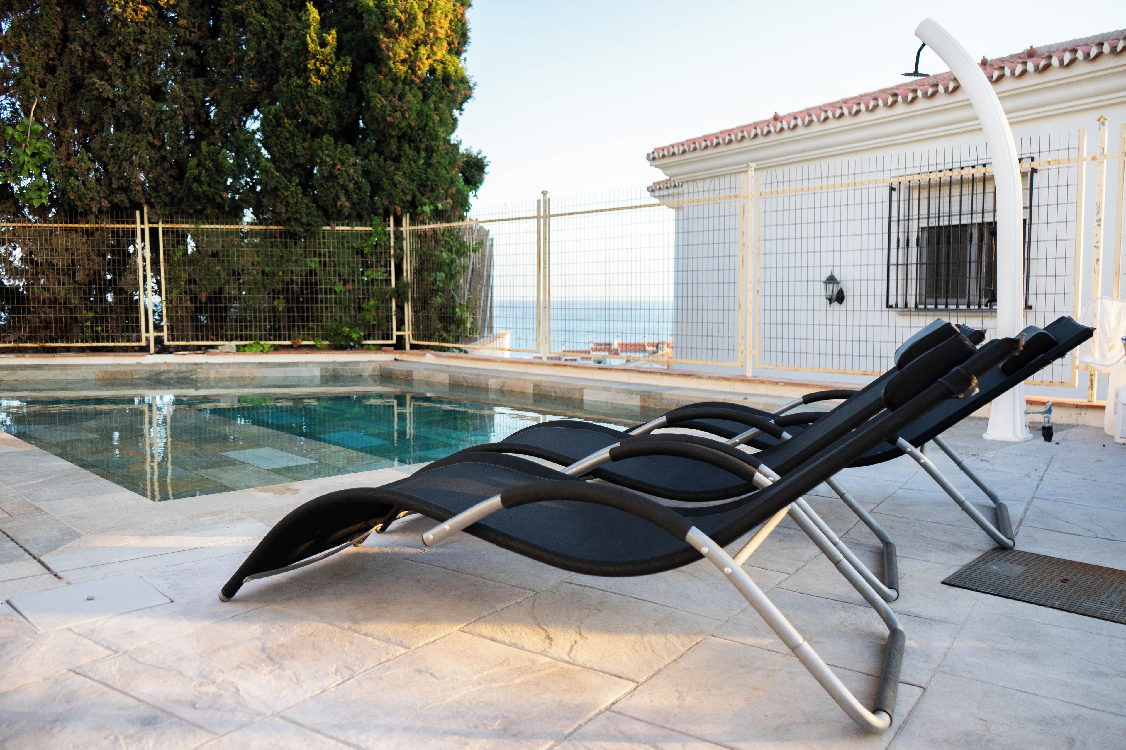 Un área junto a la piscina con sillones de descanso y una terraza con baldosas.