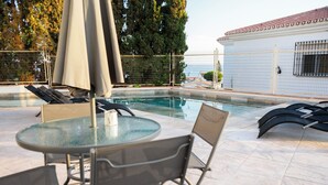 A poolside area with lounge chairs, a table, and umbrellas. - Costa del Sol Villas - Bedroom with Private Bathroom 4 (Vélez-Málaga)