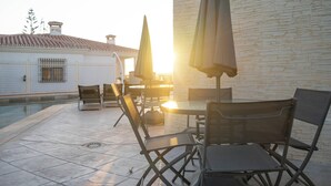 An outdoor seating area with tables and chairs, a pool, and a building with a tiled roof. - Costa del Sol Villas - Bedroom with Private Bathroom 4 (Vélez-Málaga)