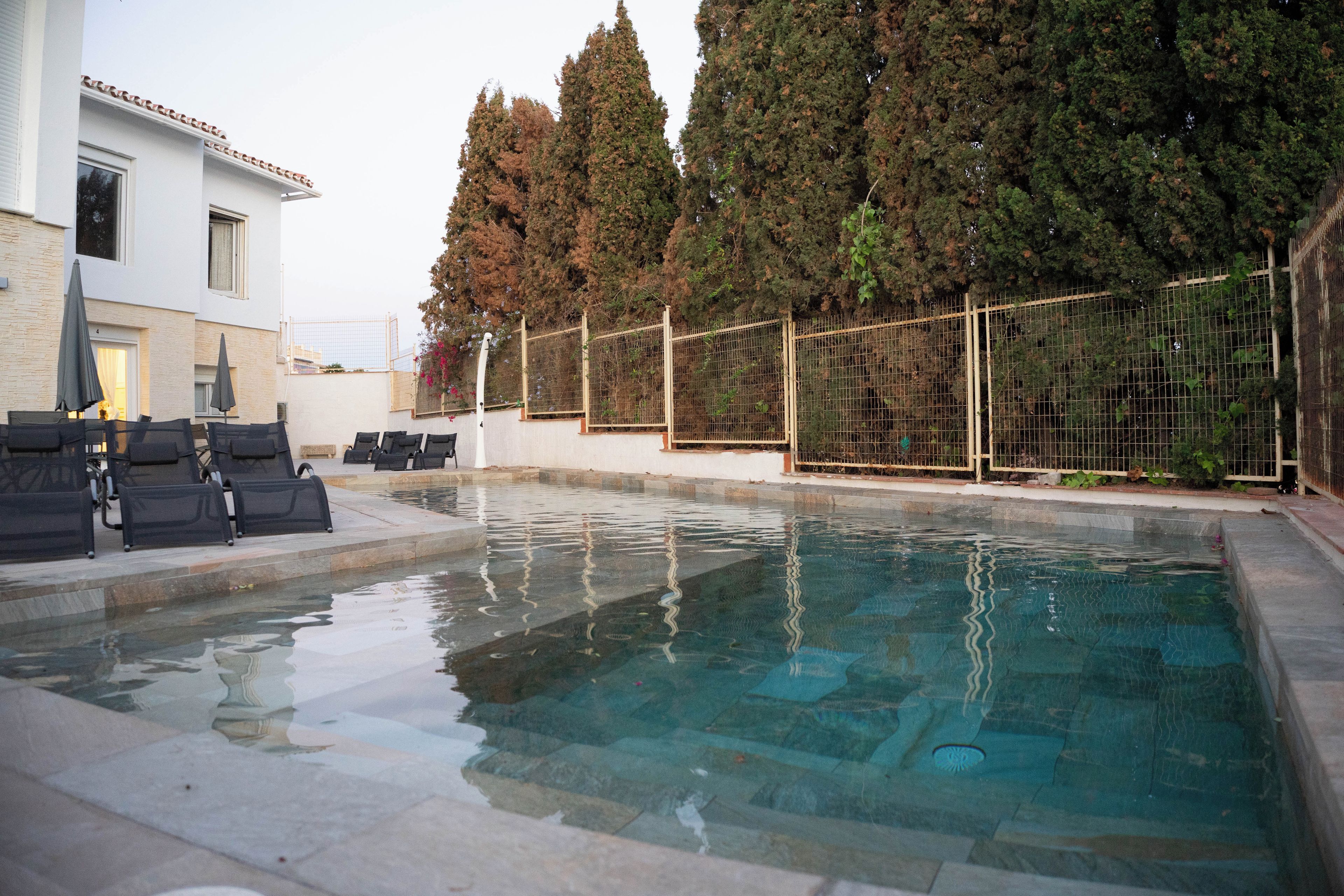 Piscina con sillas de descanso y una valla.