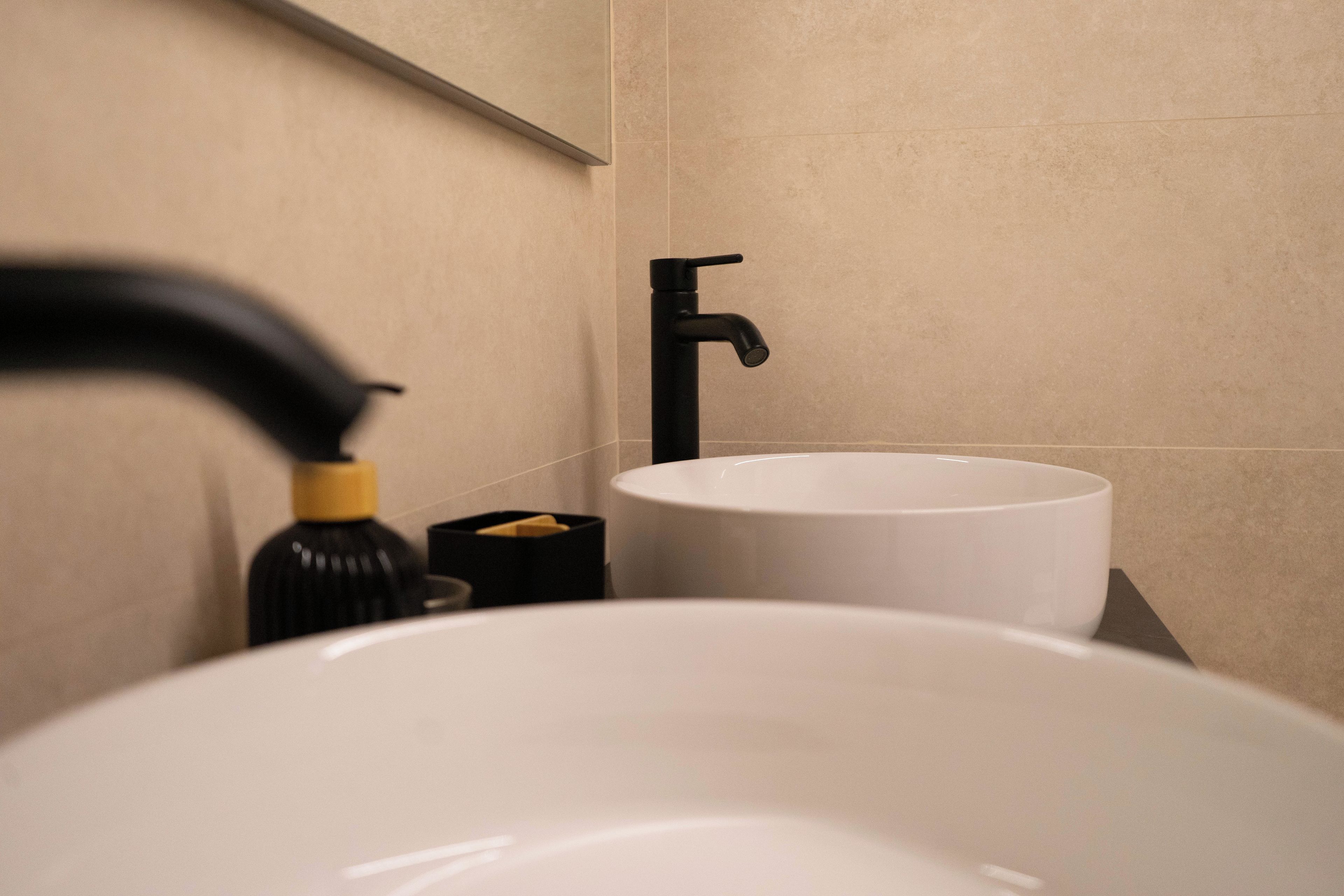 Un baño con un lavabo blanco, un grifo negro y un dispensador de jabón negro.