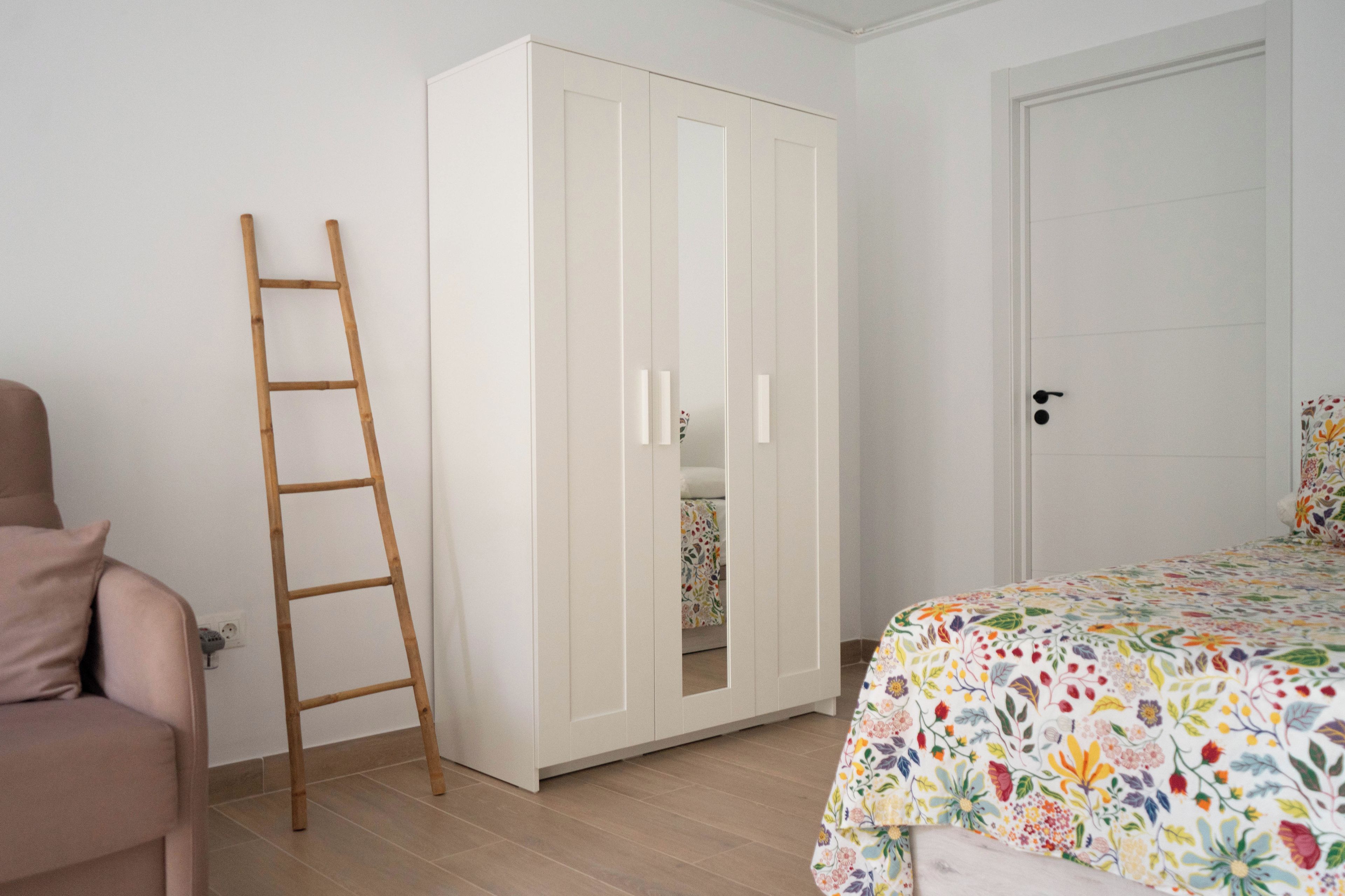 Een slaapkamer met een kledingkast, een bed met een bloemenbedekking, en een houten trap.
