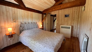 Ein Schlafzimmer mit Holzbalkendecke, einem Bett mit gemustertem Überwurf, Nachttischlampen und einem Heizkörper.