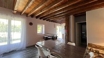 A room with a wooden ceiling, a dining table with chairs, a window, and a door leading to another room.