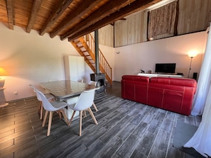 Un espai d'estar acollidor amb zona de menjador, un sofà vermell i una escala de fusta.