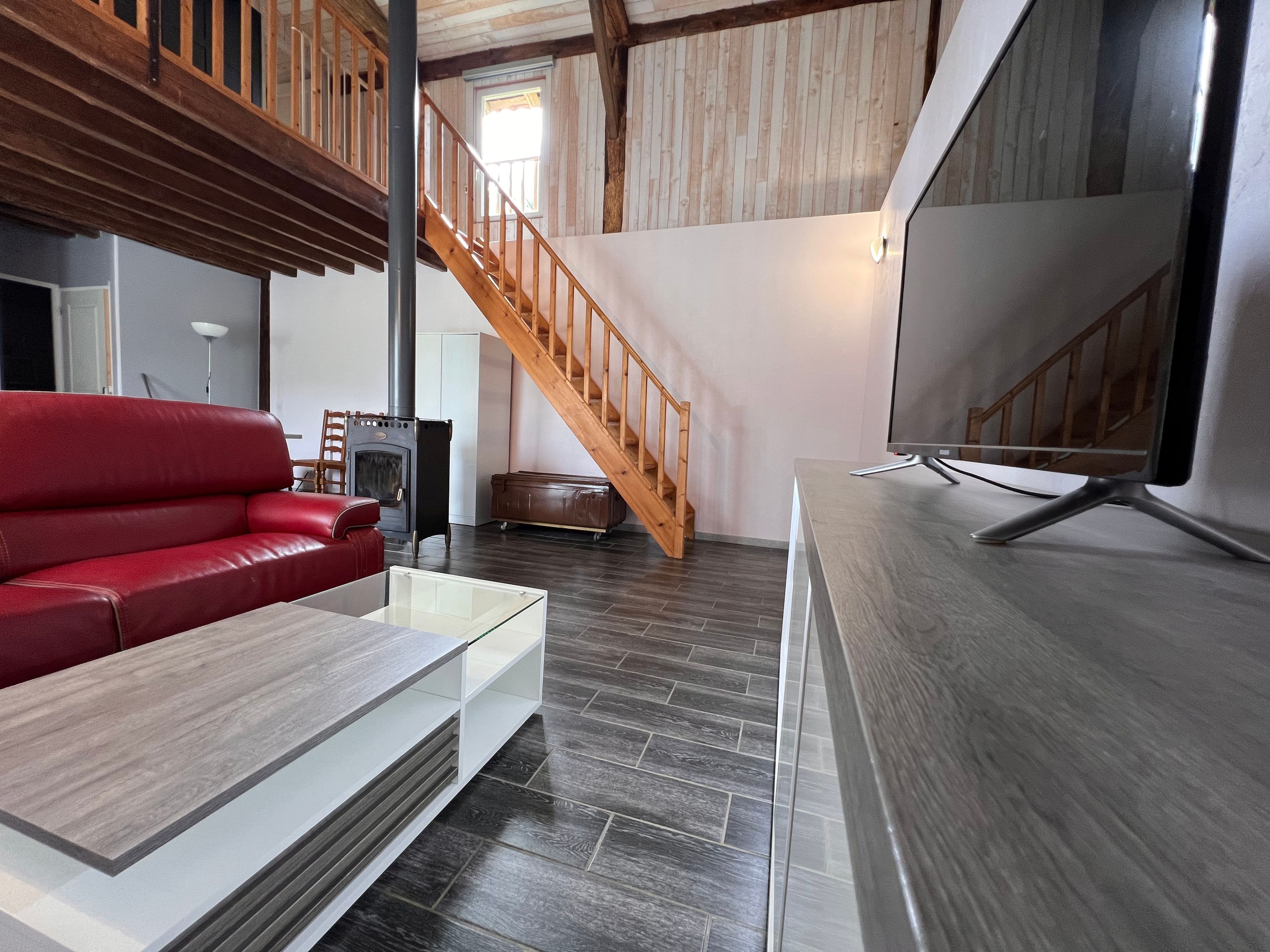 Un salon moderne avec un canapé rouge, un escalier en bois, un téléviseur et une cheminée.