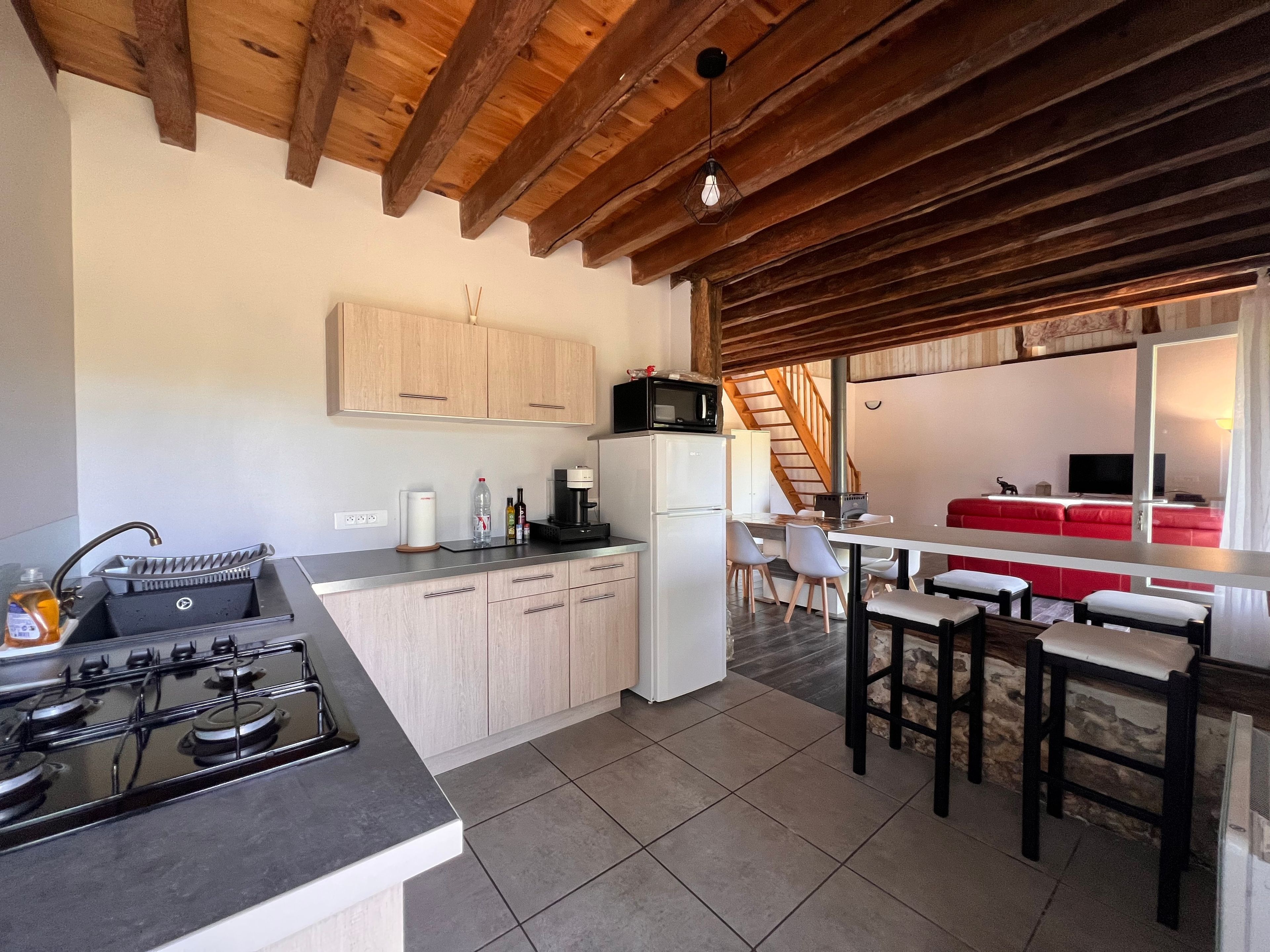 Une cuisine moderne équipée d’une cuisinière à gaz, de meubles blancs et d’un coin repas avec un canapé rouge et des chaises blanches.