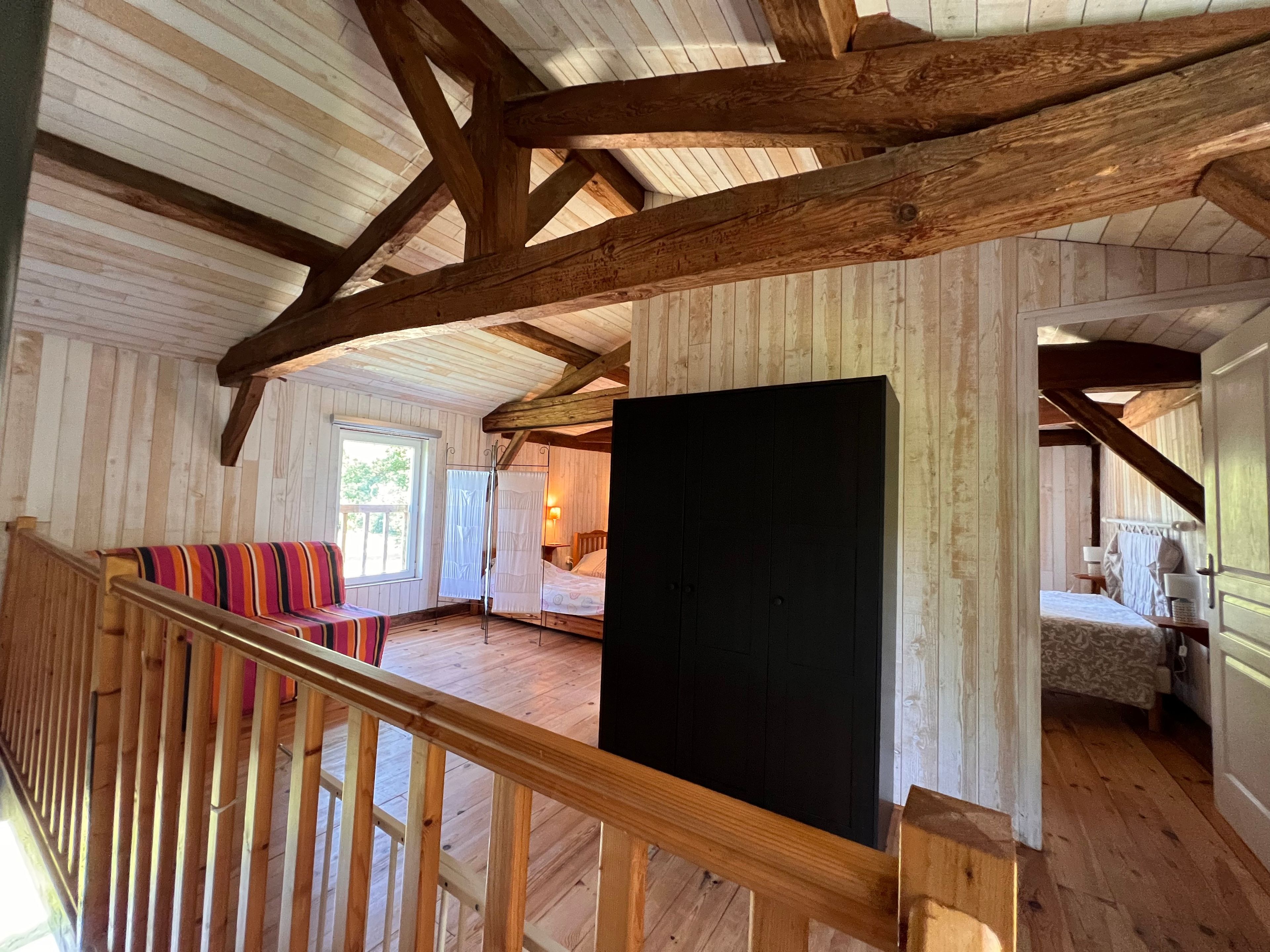 Ein geräumiges Zimmer mit Holzbalken, einem großen Bett, einer Bank und Blick ins Freie.