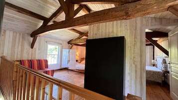 Ein geräumiges Zimmer mit Holzbalken, einem großen Bett, einer Bank und Blick ins Freie.