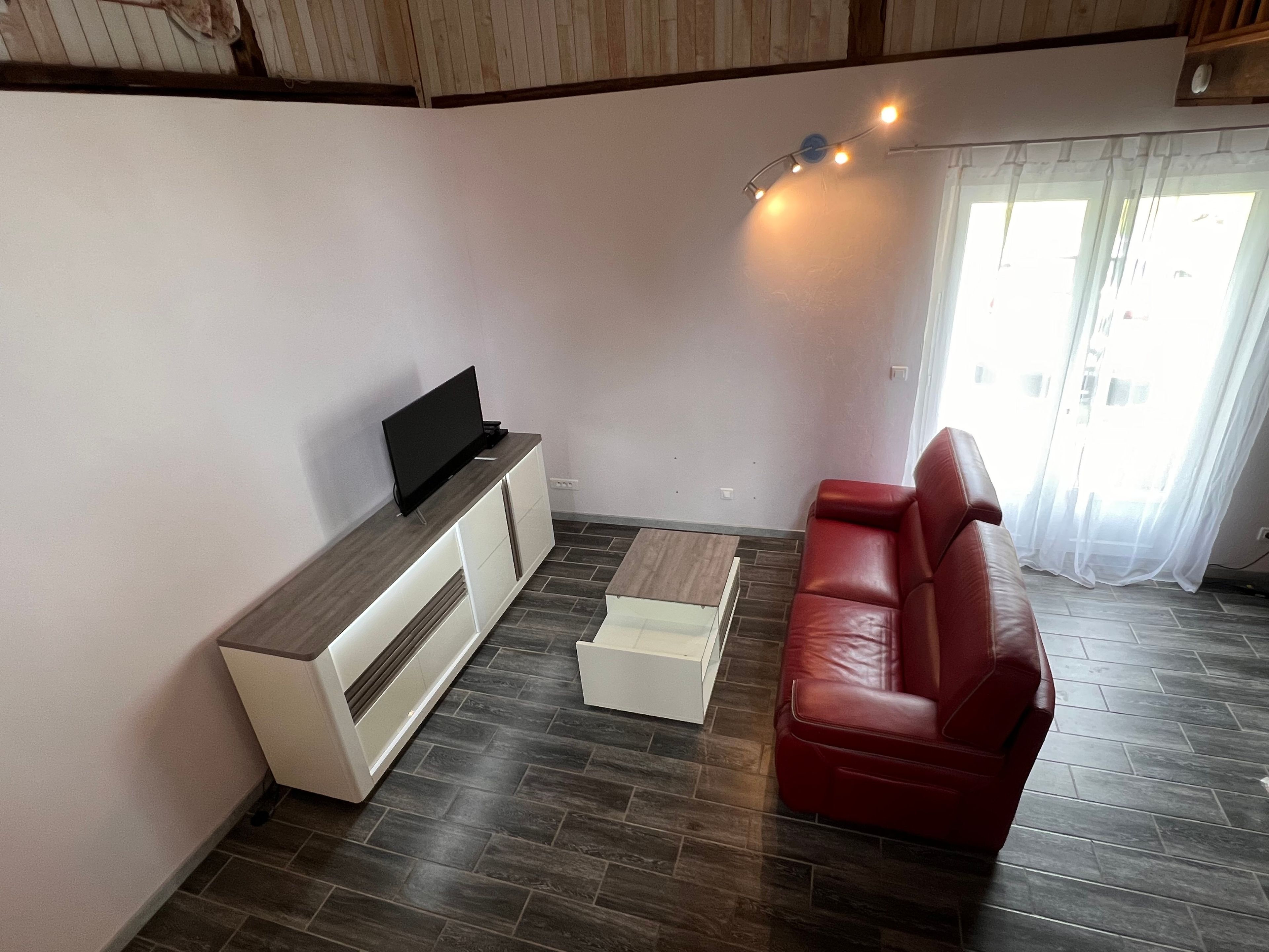 Un soggiorno con una TV a schermo piatto su un mobile in legno, un divano in pelle rossa, un tavolino da caffè e una lampada a sospensione.