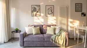A living room with a sofa, two pillows, a small table with a plant, and a chair. There are two framed artworks on the wall and a radiator. - Casa Michela - 20 minutes to the city center (Scandicci)