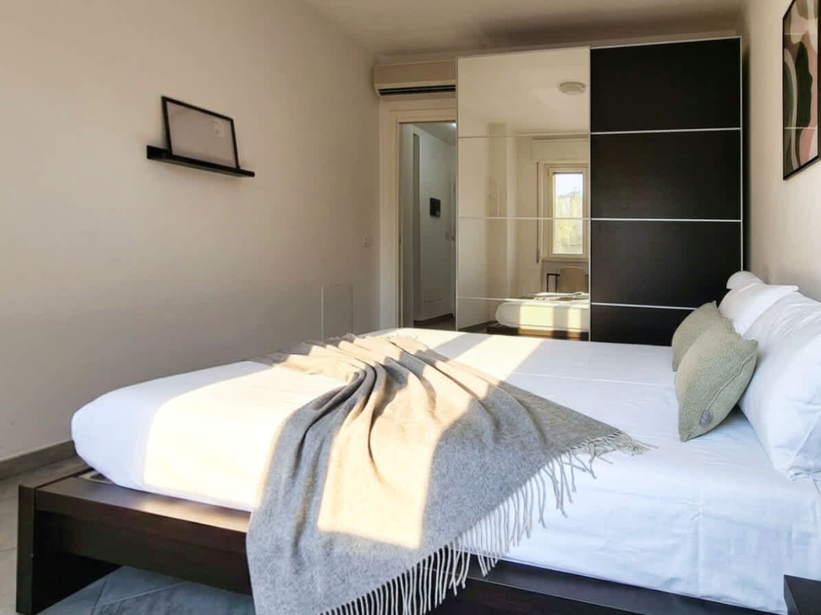 Ein Schlafzimmer mit einem Bett, einem Nachttisch, einem Spiegel und einer Tür zu einem anderen Raum.