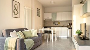 A modern living room with a grey sofa, a dining table with chairs, and a kitchen area with white cabinets and appliances. - Casa Michela - 20 minutes to the city center (Scandicci)
