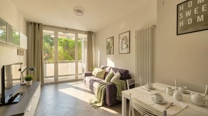 A modern living room with a sofa, dining table set for tea, and a view through a sliding glass door. - Casa Michela - 20 minutes to the city center (Scandicci)