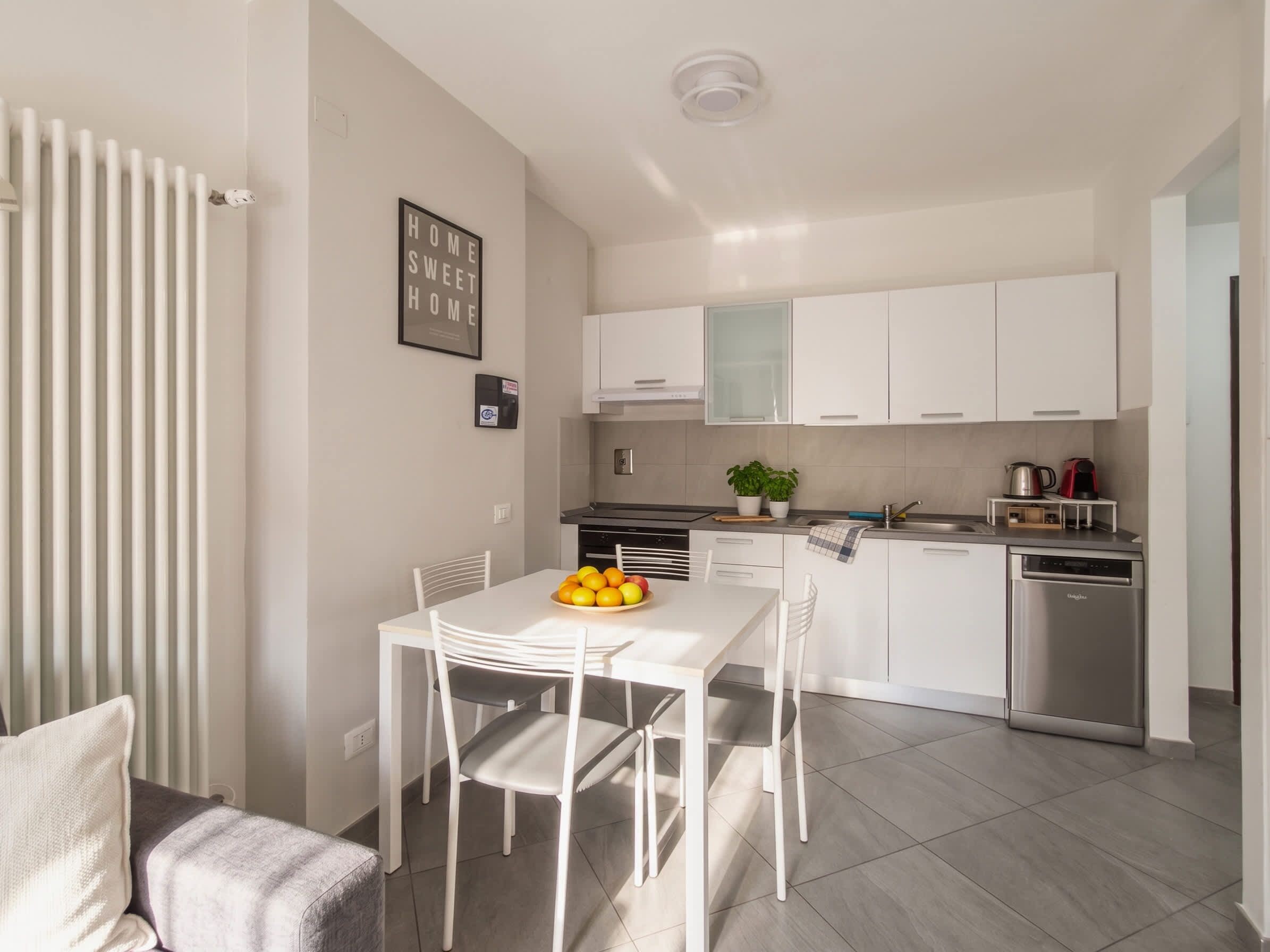 Una cucina moderna con mobili bianchi, lavastoviglie e zona pranzo con tavolo e sedie bianche.