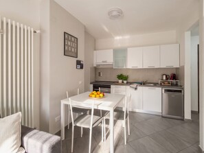 A modern kitchen with white cabinets, a dishwasher, and a dining area with a white table and chairs. - Casa Michela - 20 minutes to the city center (Scandicci)