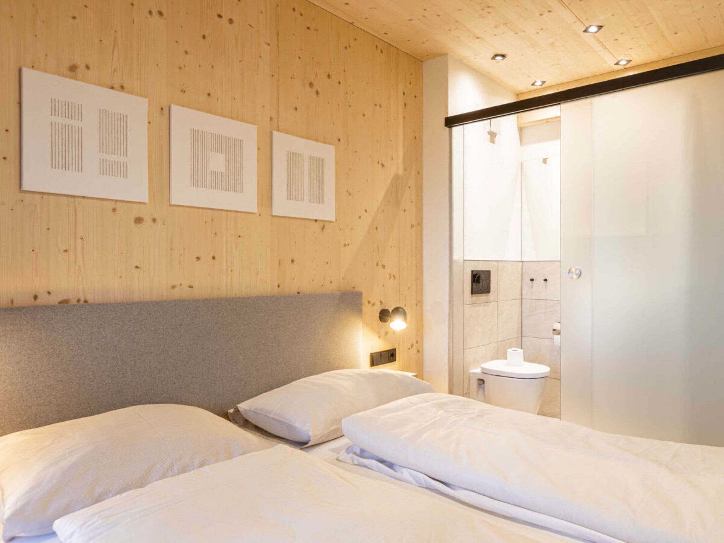 A hotel room with a wooden ceiling, a bed with white bedding, and a wall-mounted light fixture.