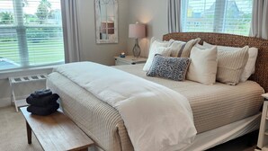 Quarto com uma cama grande, mesas de cabeceira, um banco e uma janela com cortinas.