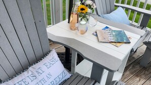 Um terraço com cadeiras Adirondack cinzentas, uma mesa pequena e uma almofada com texto.