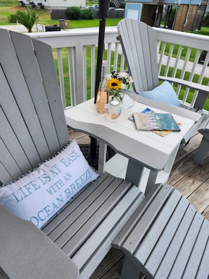 Una terraza con sillas Adirondack grises, una mesita y un cojín con texto.