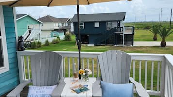A wooden deck with two Adirondack chairs, a small table, and a beige umbrella.