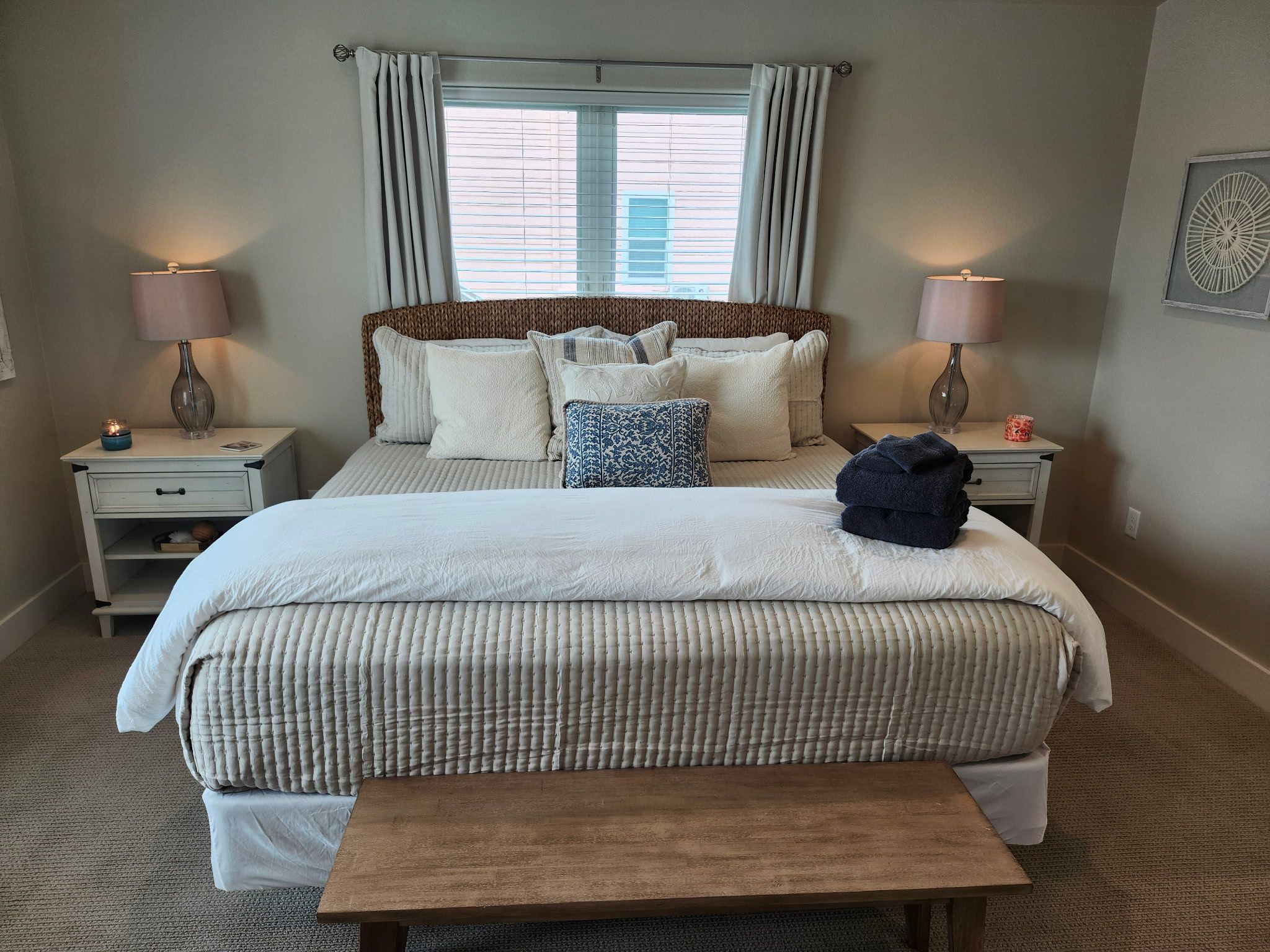 A bedroom with a large bed, two bedside tables, a nightstand, a bench, and a window with curtains.