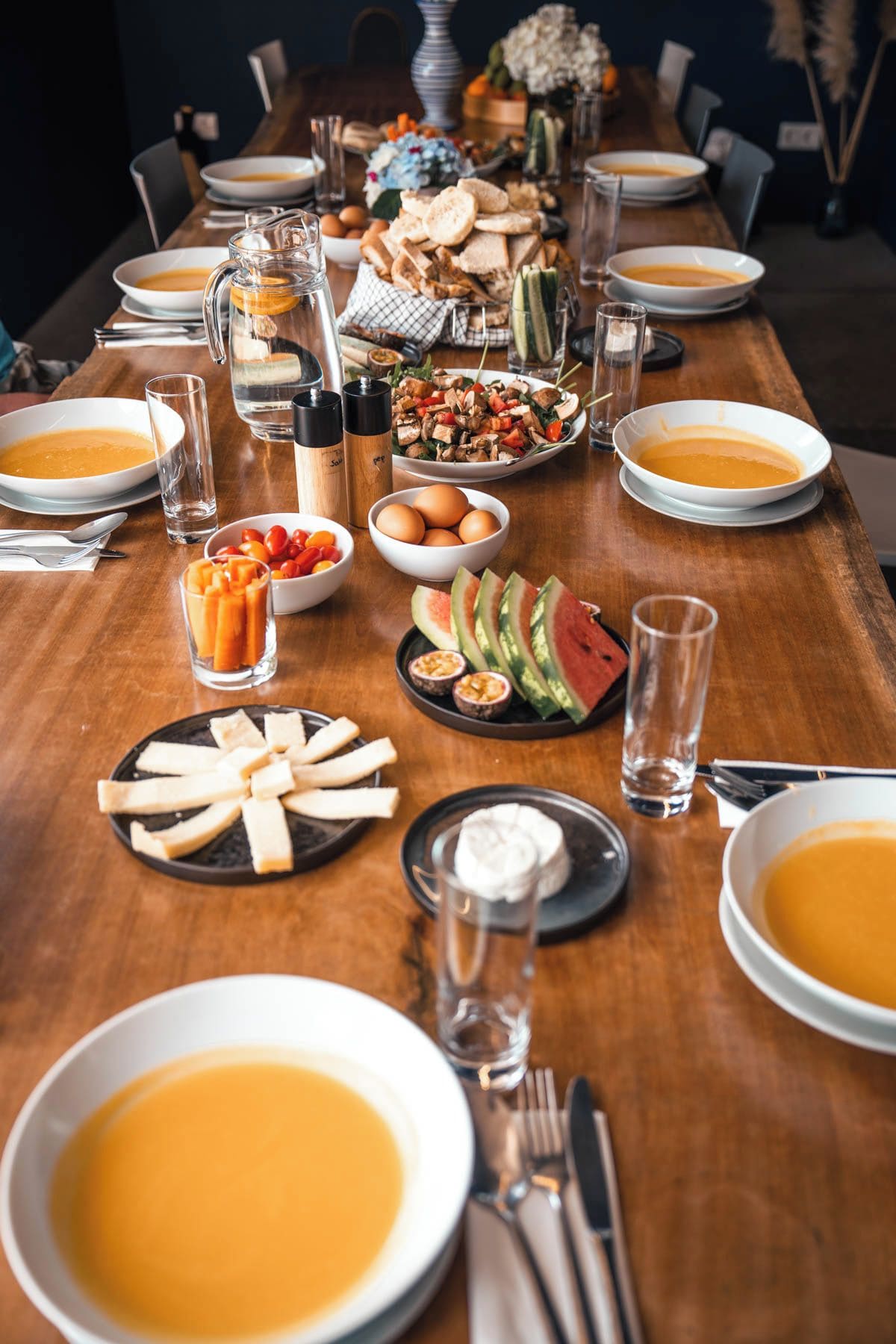 Ein langer Esstisch, reichhaltig gedeckt mit verschiedenen Speisen, darunter Suppe, Salat und Brot.