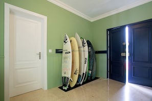 A hallway with a row of surfboards leaning against the wall, a white door, and a dark blue door. - Salt Lips (Ponta Delgada)