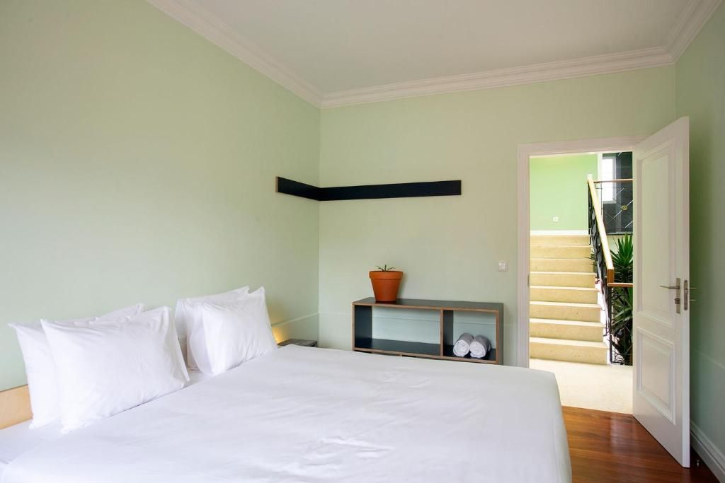 A bedroom with a bed, a nightstand, a shelf with a potted plant, and a door leading to a staircase.