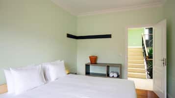 A bedroom with a bed, a nightstand, a shelf with a potted plant, and a door leading to a staircase.