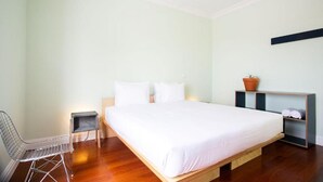 Ein Schlafzimmer mit einem Bett, einem Sessel, einem kleinen Tisch und einem Regal mit einer Pflanze.