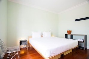 A bedroom with a bed, a chair, a small table, and a shelf with a plant. - Salt Lips (Ponta Delgada)