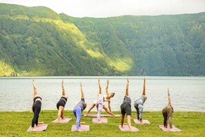 A group of people performing yoga on mats by a lake with a forested hill in the background. - Salt Lips (Ponta Delgada)